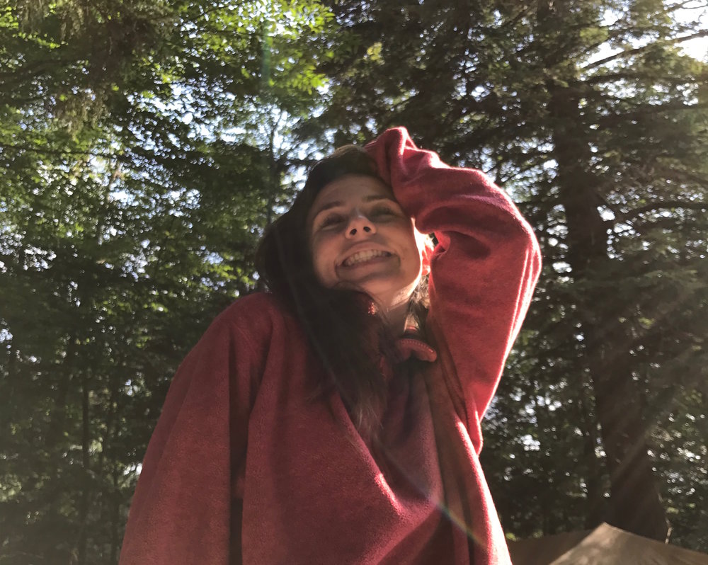Kay smiling in the woods wearing a pink sweater